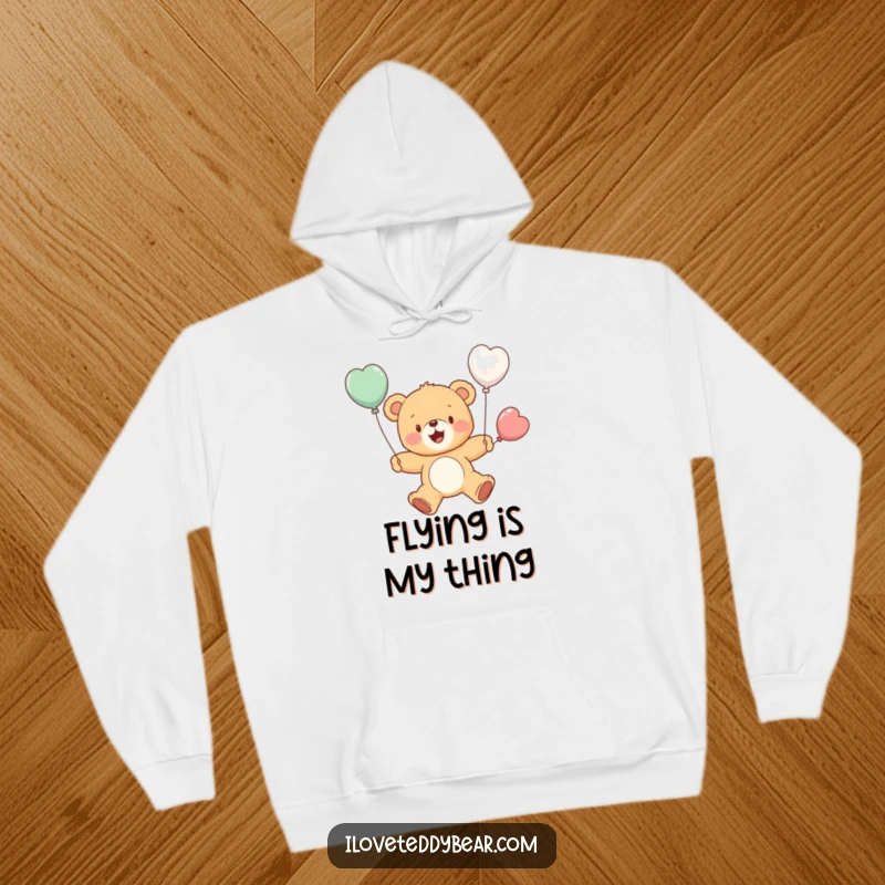 Funny hoodie depicting a cheerful teddy bear bravely attempting to fly with small balloon wings, a humorous and inspiring scene. A great funny gift.